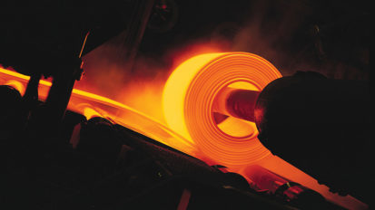 a large hot orange steel sheet is being rolled by a machine in a steel mill